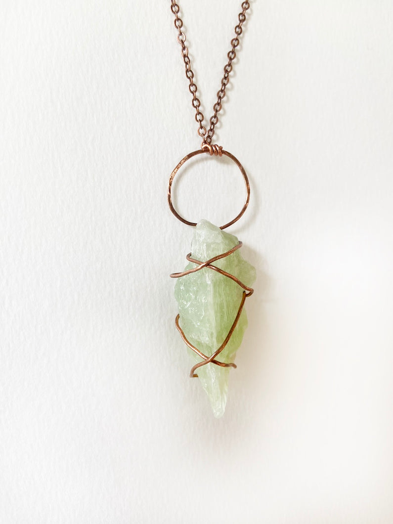 Pale Light Lime Green Calcite Wire-Wrapped Copper Pendant Necklace. Genuine Real Raw Crystal Gemstone Sourced in Asheville, North Carolina. Minimalist Modern Bohemian Style with Criss-Cross X Design. Authentic One-of-a-Kind Handmade Jewelry.