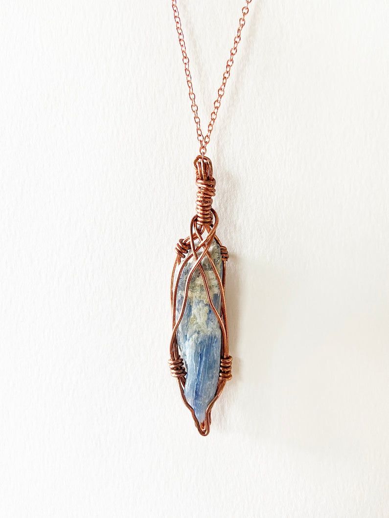 Blue Kyanite Wire-Wrapped Copper Pendant Necklace. Genuine Real Raw Crystal Gemstone Sourced in Asheville, North Carolina. Minimalist Modern Bohemian Style with Criss-Cross Design. Authentic One-of-a-Kind Handmade Jewelry.